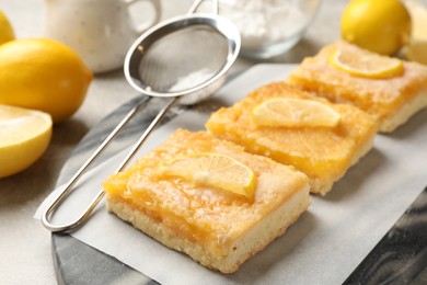 Photo of Tasty lemon bars and sieve on table, closeup