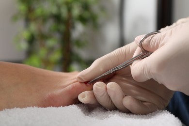 Pedicurist cutting client`s toenails with scissors in beauty salon, closeup