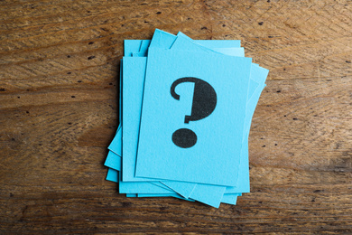 Blue paper cards with question mark on wooden background, top view