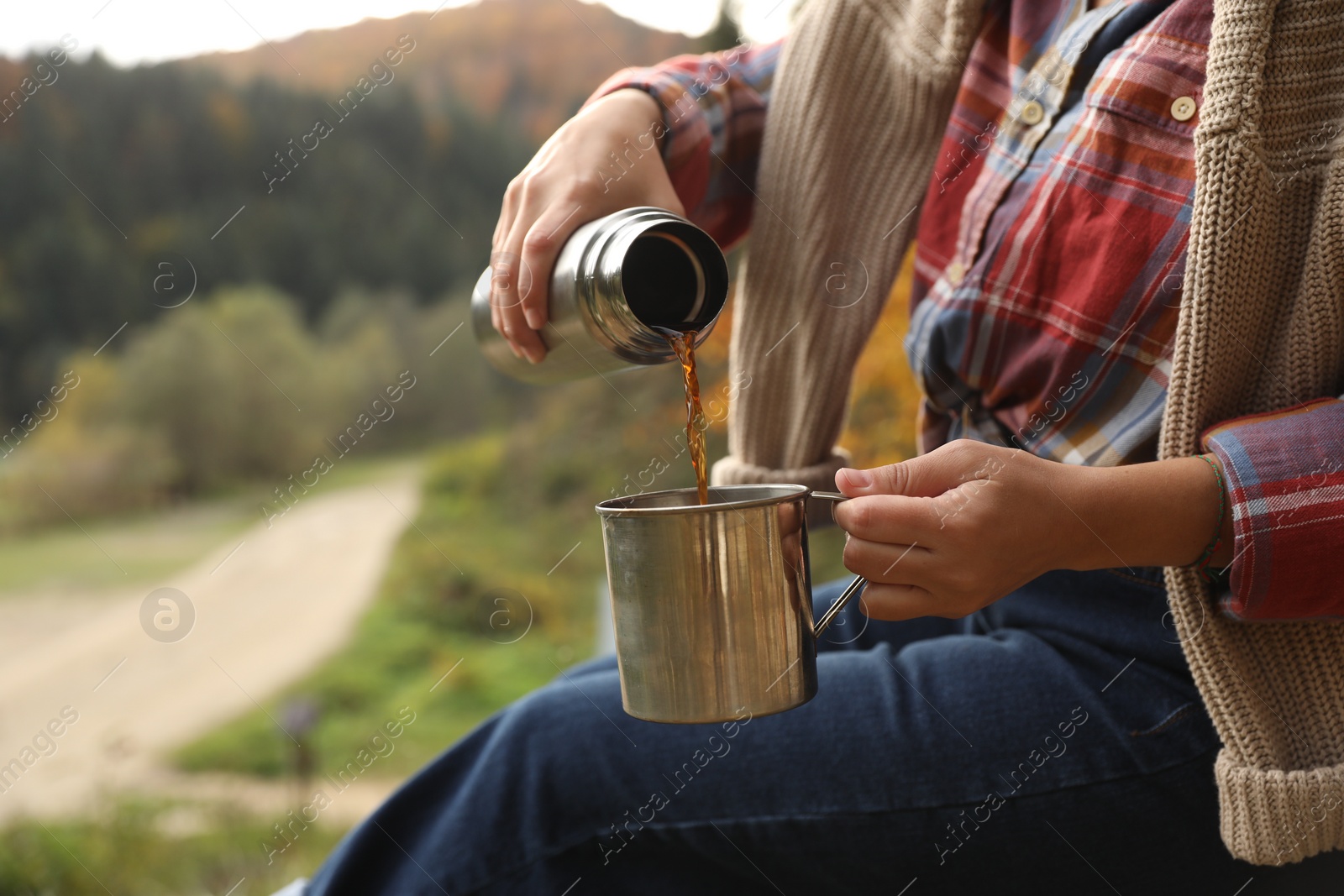 Photo of Woman pouring hot drink from thermos into metallic mug outdoors, closeup. Space for text