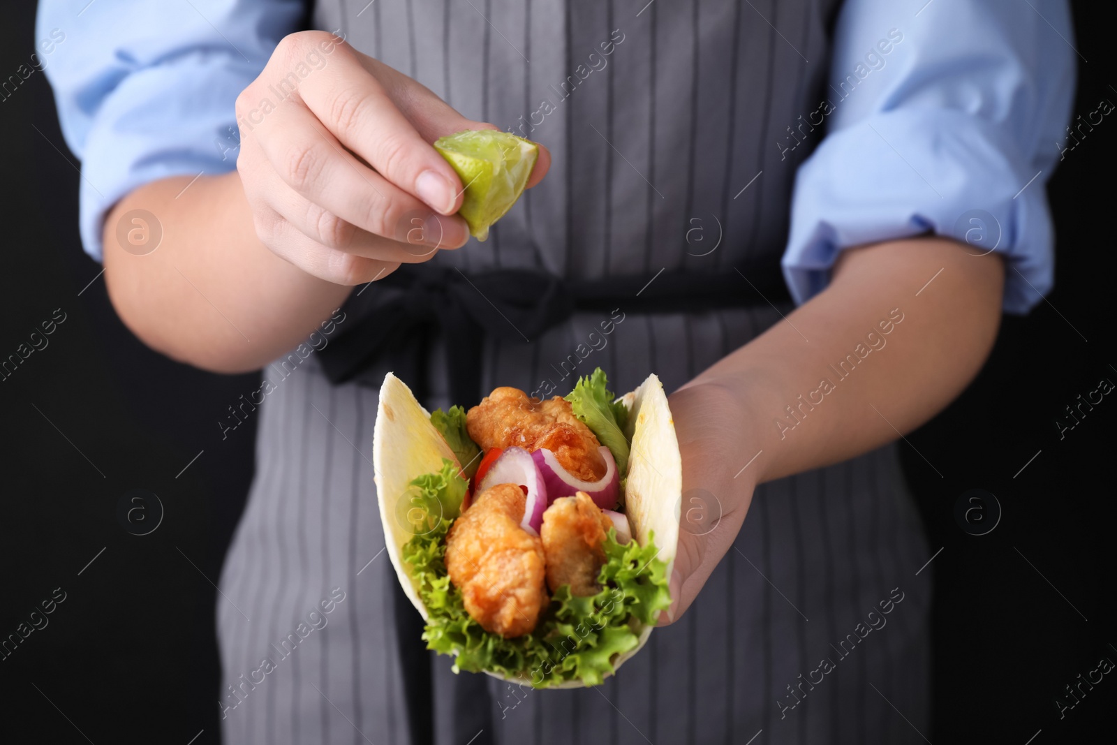 Photo of Woman squeezing lime on fish taco against dark background, closeup