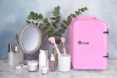 Photo of Cosmetic refrigerator and skin care products on white marble table