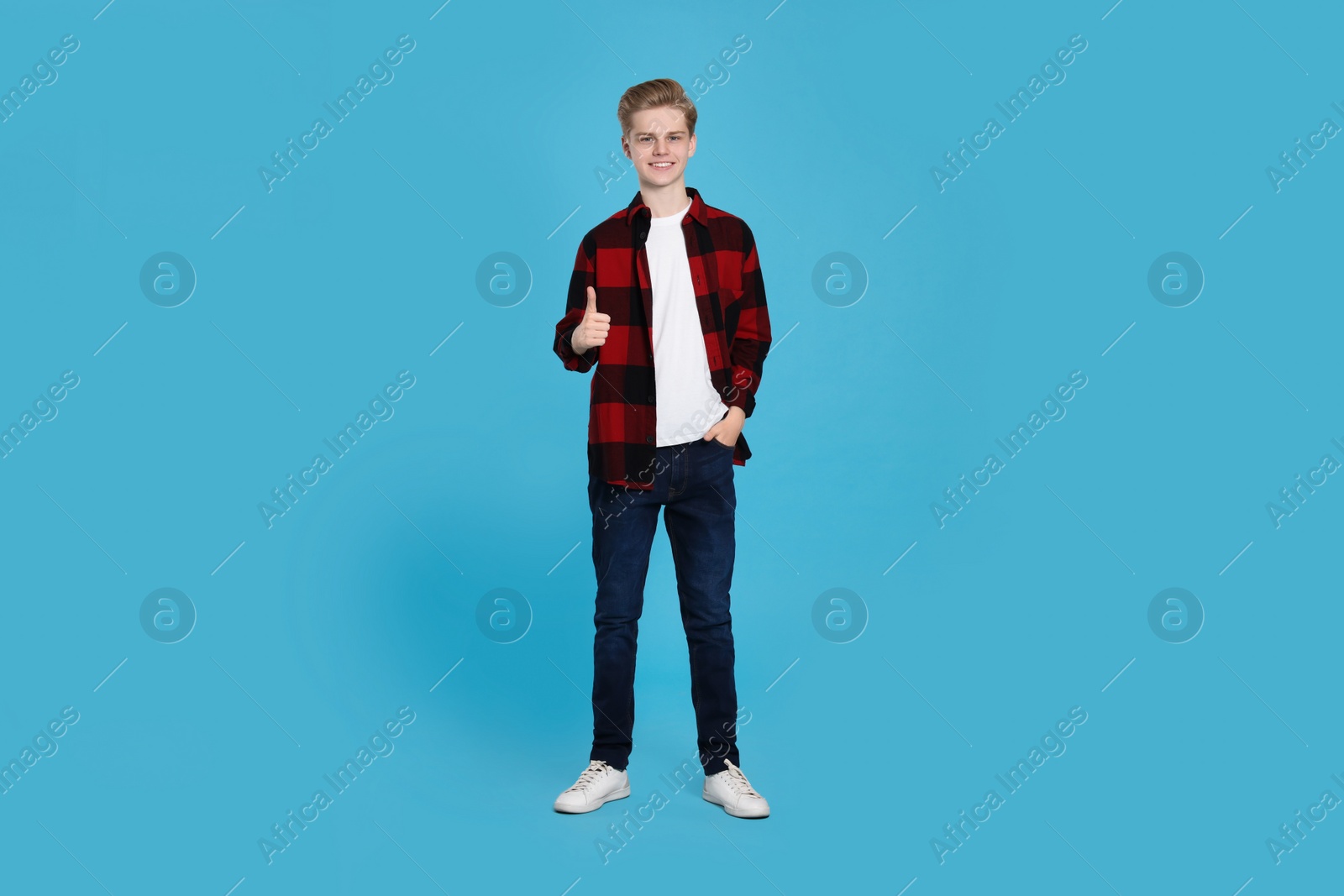 Photo of Teenage boy showing thumb up on light blue background