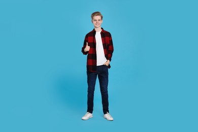 Teenage boy showing thumb up on light blue background