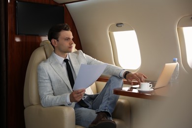 Photo of Businessman with documents working on laptop at table in airplane during flight
