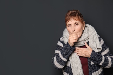 Photo of Elderly woman coughing against dark background. Space for text