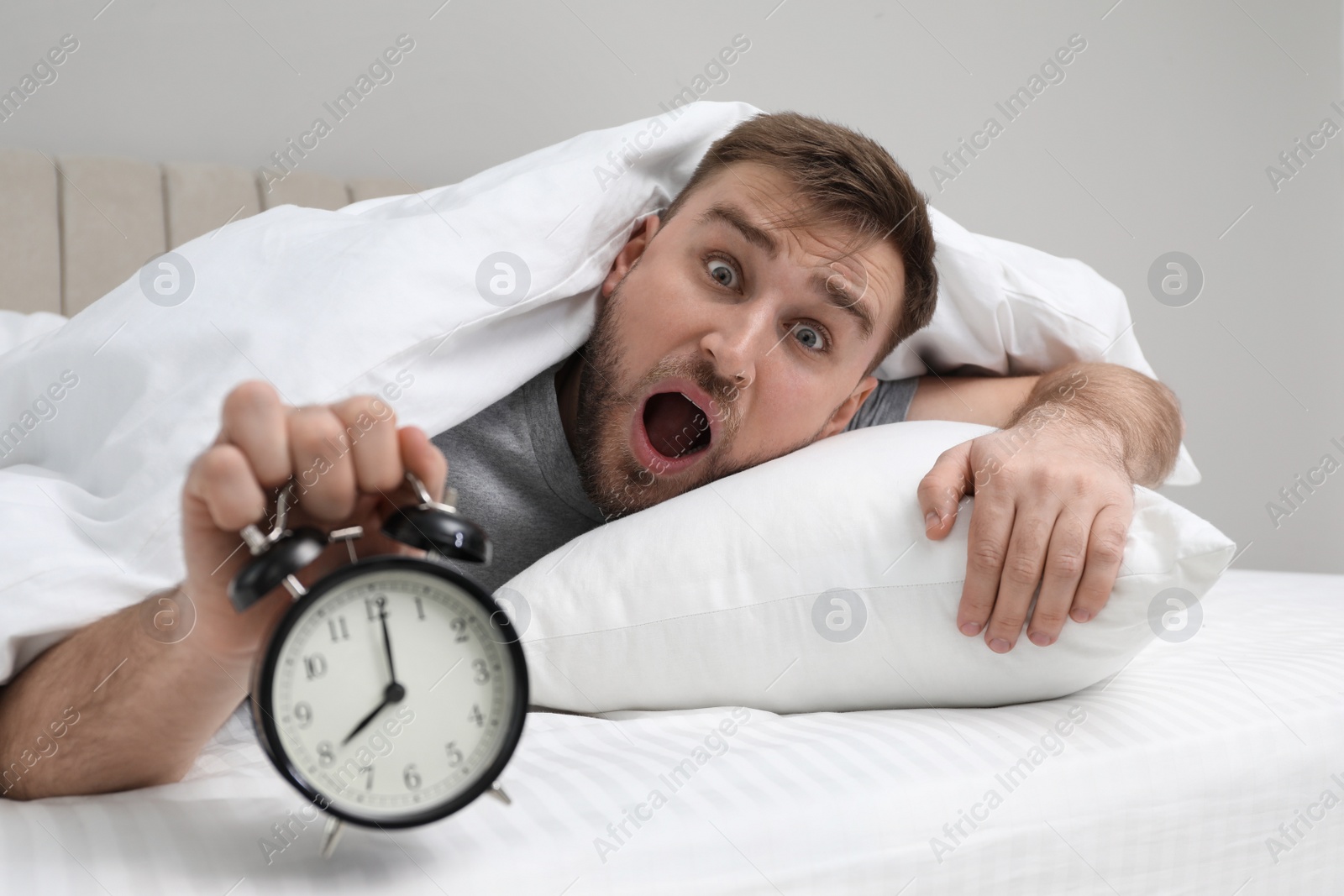 Photo of Emotional overslept man with alarm clock in bed. Being late concept