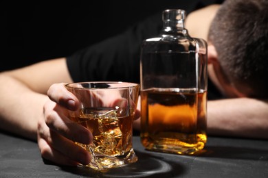 Photo of Alcohol addiction. Man with whiskey at dark textured table, selective focus