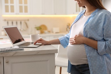Photo of Pregnant woman working in kitchen at home, closeup. Maternity leave