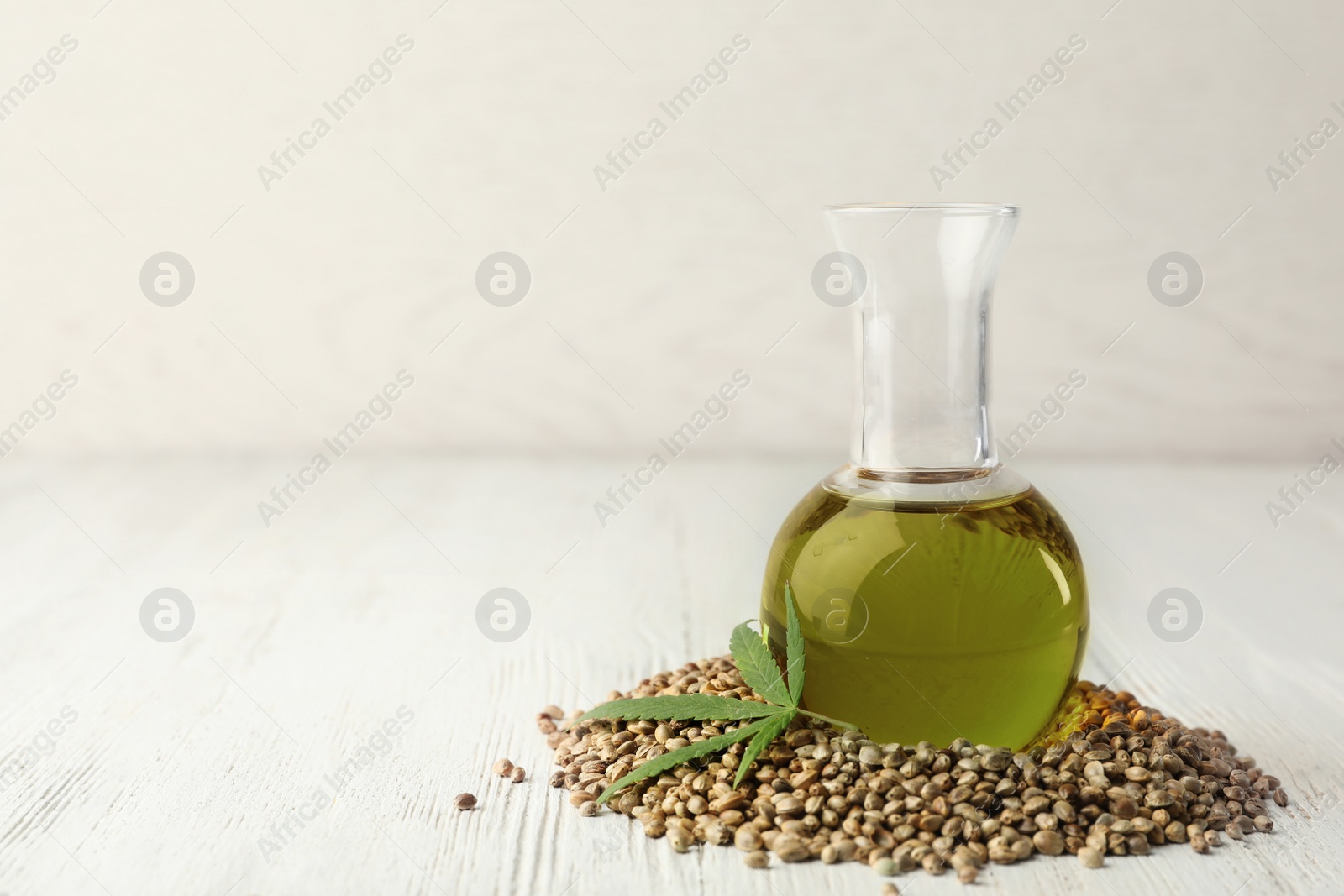 Photo of Hemp oil, seeds and leaf on white wooden table. Space for text