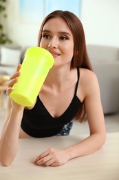 Young woman drinking protein shake at table indoors