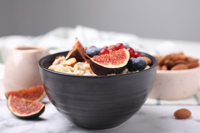 Photo of Bowl of oatmeal with berries, almonds and fig pieces on white marble table, closeup