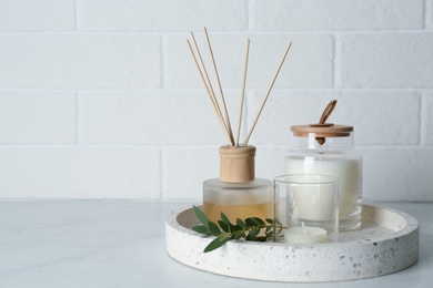 Photo of Candles, eucalyptus branch and aromatic reed air freshener on white table near brick wall, space for text. Interior elements
