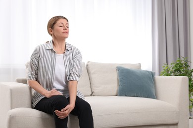 Woman suffering from knee pain on sofa indoors. Arthritis symptoms