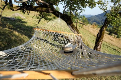 Photo of Comfortable net hammock with hat and book in mountains on sunny day