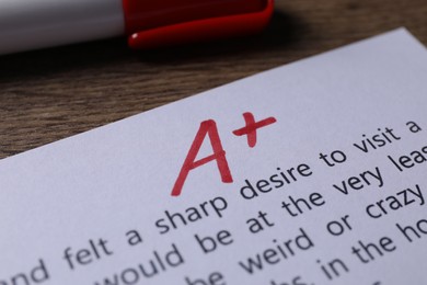 School grade. Sheet of paper with red letter A, plus symbol and marker on wooden table, closeup