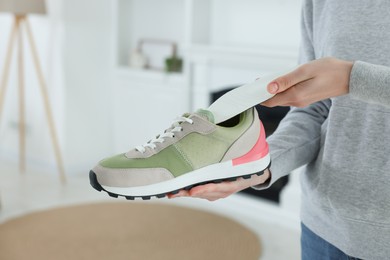 Woman putting orthopedic insole into shoe at home, closeup. Foot care