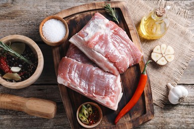 Photo of Pieces of raw pork belly, oil, garlic, salt and spices on wooden table, flat lay