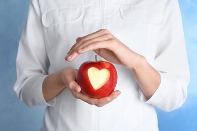 Photo of Woman holding apple with carved heart on color background, closeup