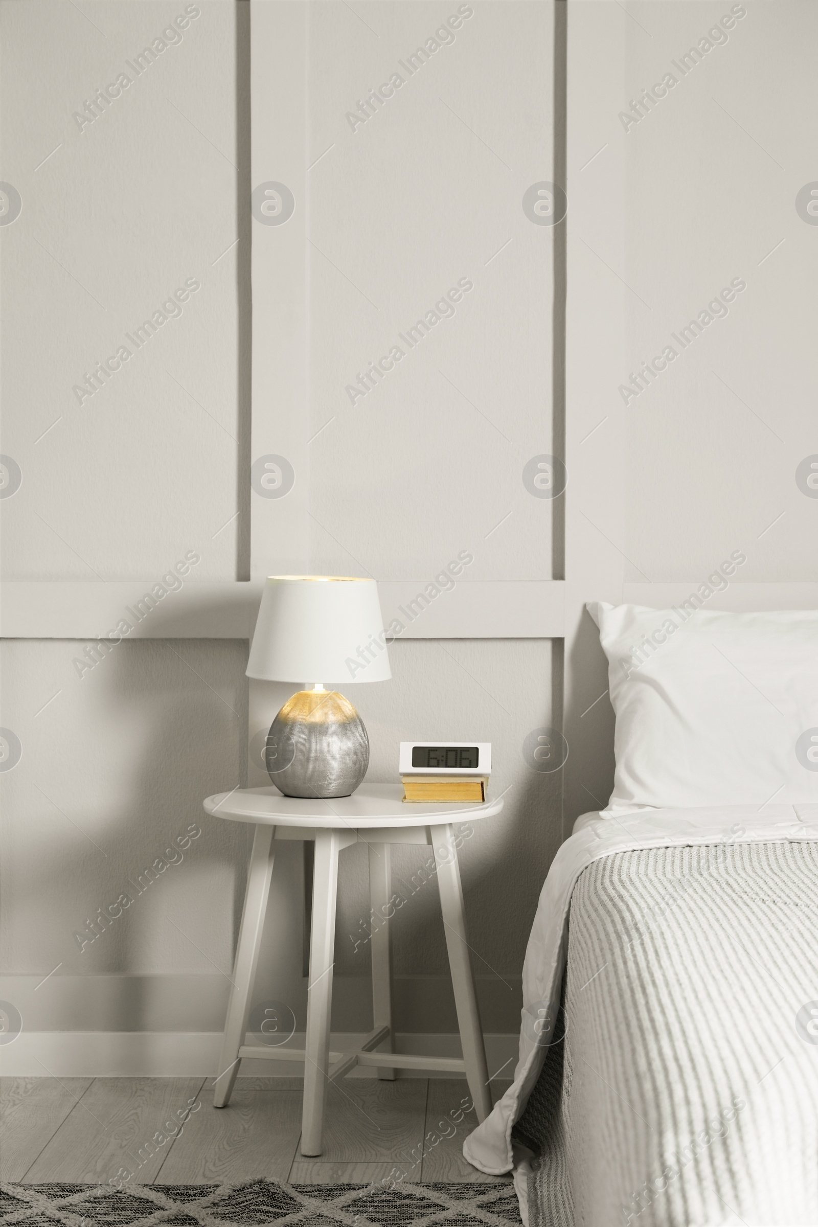 Photo of Stylish lamp, alarm clock and book on bedside table indoors. Bedroom interior elements