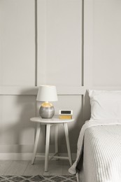 Photo of Stylish lamp, alarm clock and book on bedside table indoors. Bedroom interior elements