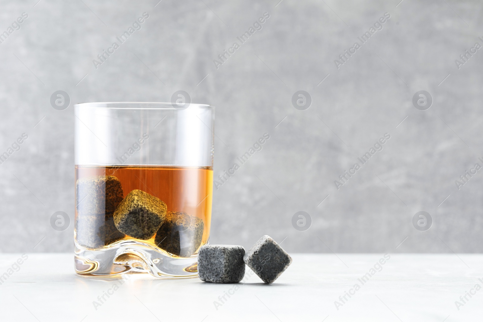 Photo of Whiskey stones and drink in glass on light marble table. Space for text