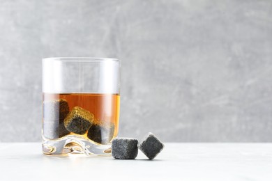 Whiskey stones and drink in glass on light marble table. Space for text