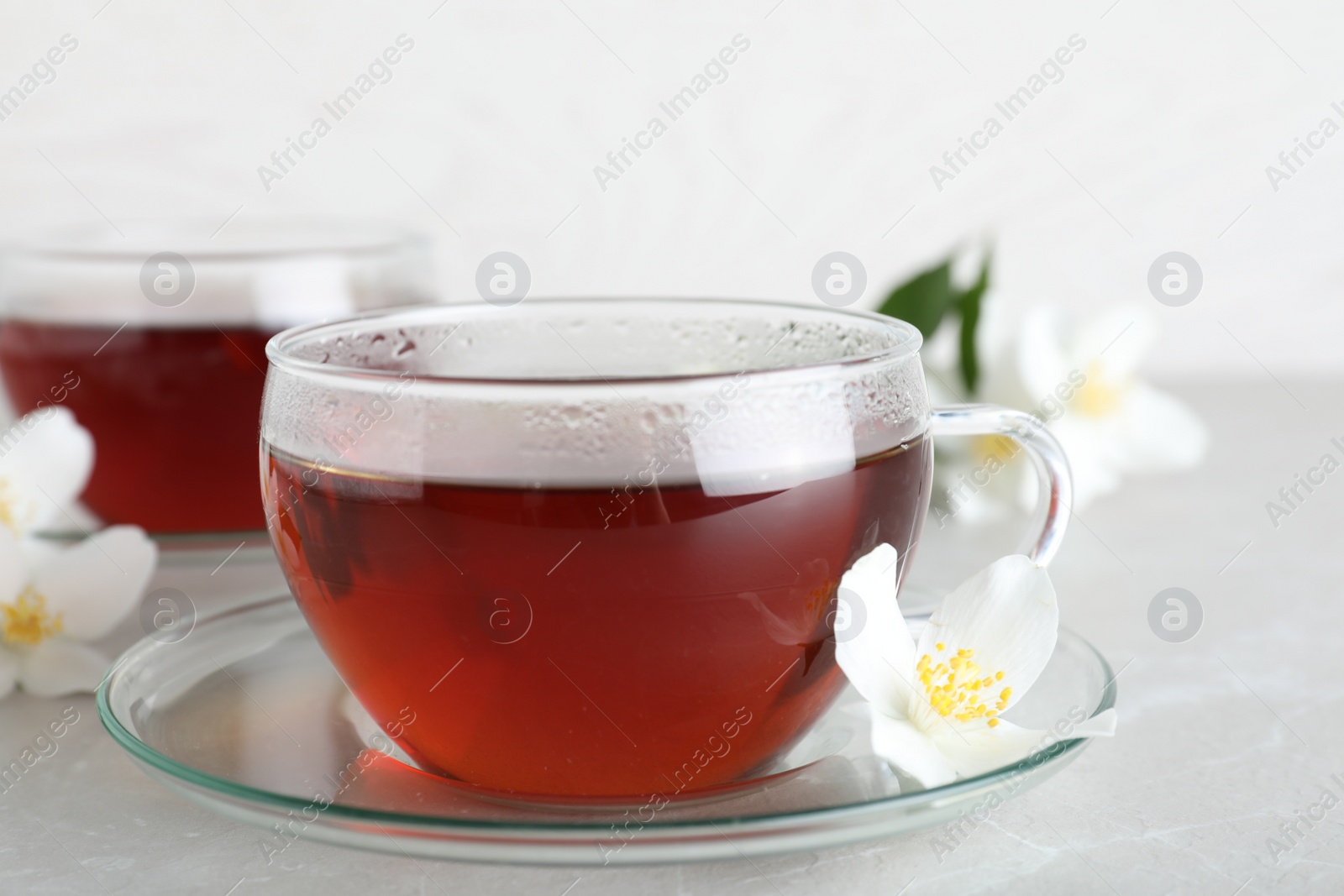 Photo of Cup of tea and fresh jasmine flower on light grey marble table