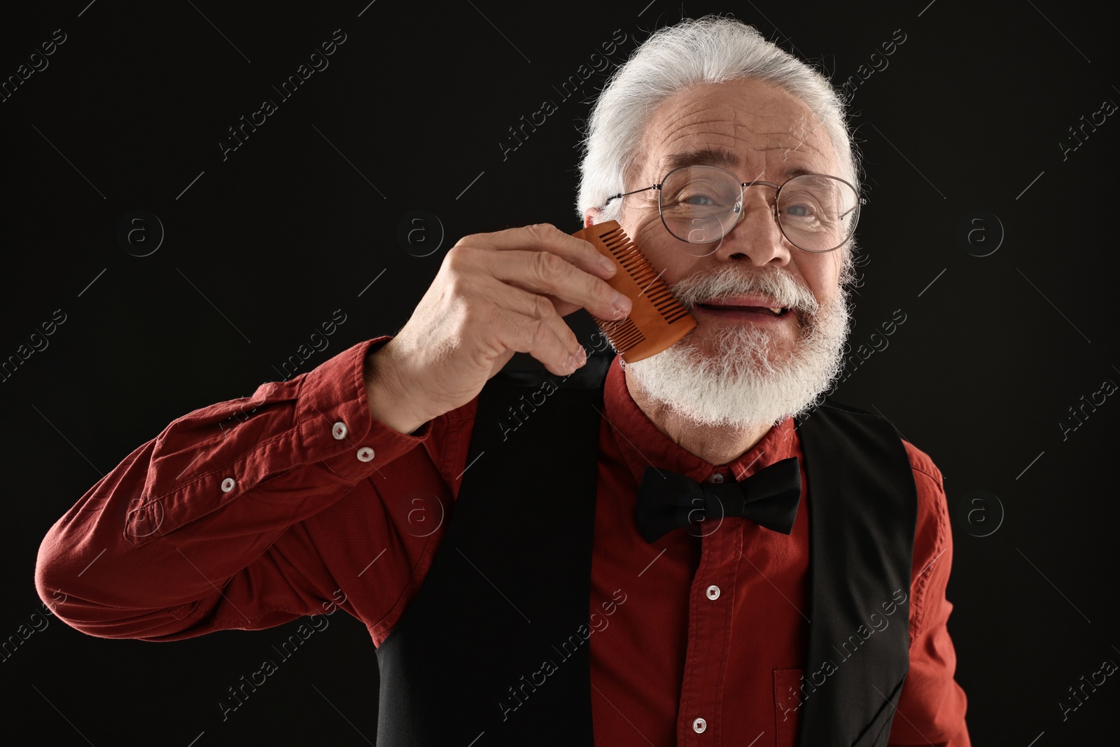 Photo of Senior man combing mustache on black background