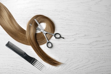 Photo of Flat lay composition with hair lock and tools on wooden background. Space for text