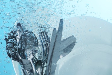 Washing silver cutlery and plates in water on light blue background