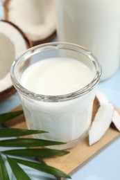 Photo of Glass of delicious vegan milk, coconuts and leaf on light blue background, closeup