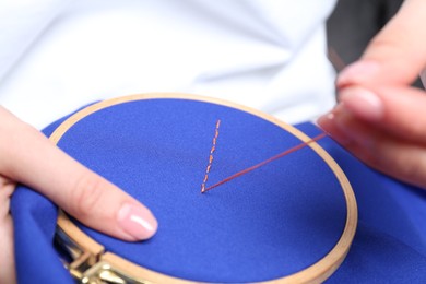 Photo of Woman with sewing needle and thread embroidering on cloth, closeup