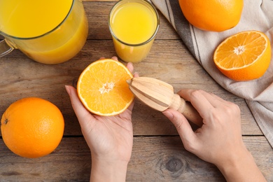 Photo of Woman squeezing orange juice at wooden table, top view
