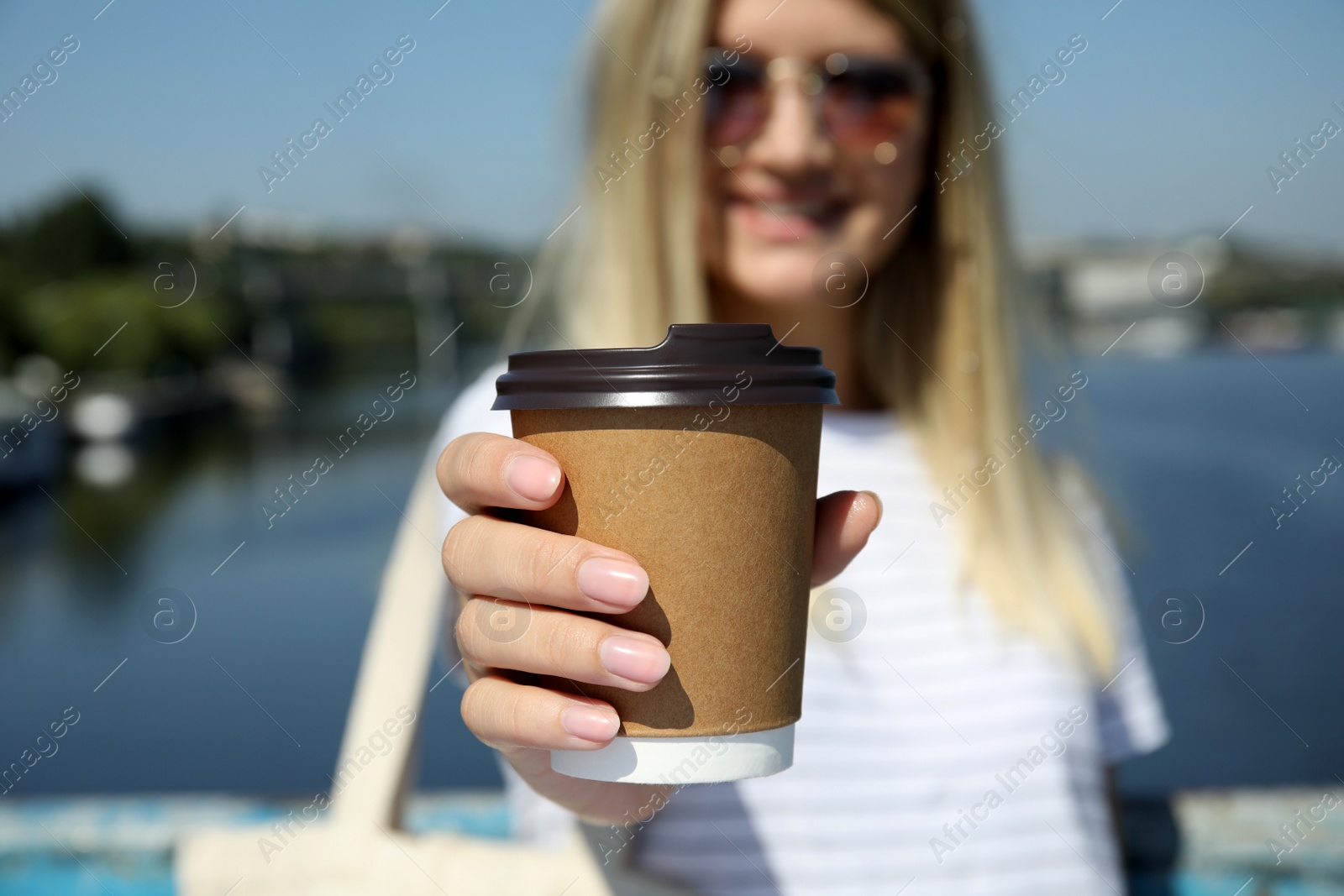 Photo of Woman holding takeaway cardboard coffee cup with plastic lid outdoors, closeup