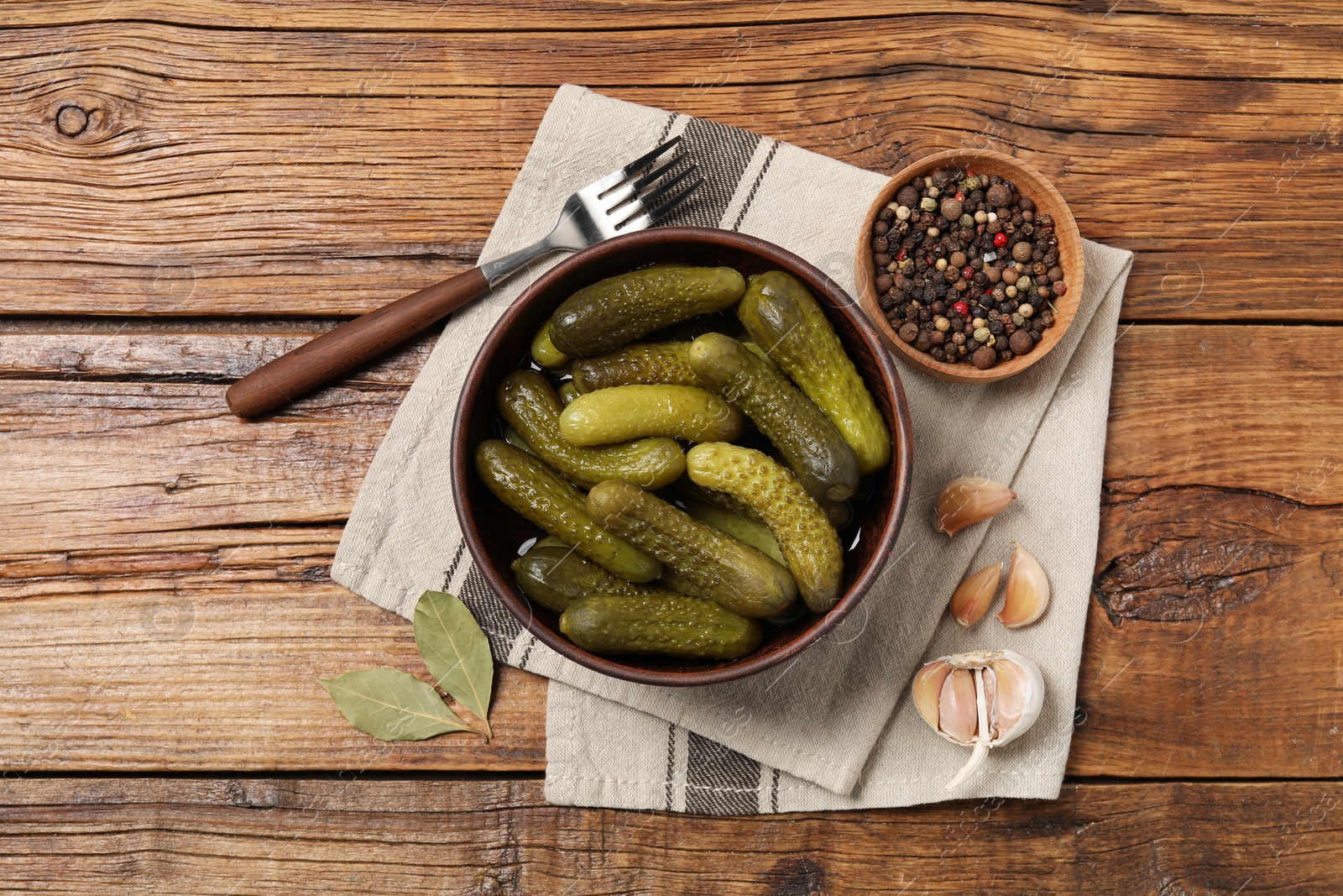 Photo of Tasty pickled cucumbers in bowl, fork and ingredients on wooden table, flat lay