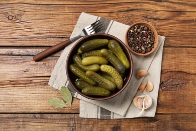 Photo of Tasty pickled cucumbers in bowl, fork and ingredients on wooden table, flat lay