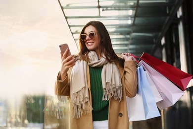 Image of Stylish woman with phone and shopping bags after visiting fashion buyer outdoors