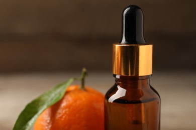 Photo of Bottle of tangerine essential oil and fresh fruit on blurred background, closeup