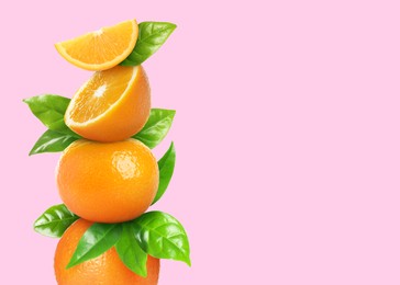 Image of Stacked cut and whole oranges with green leaves on pale pink background, space for text
