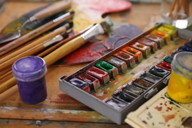 Photo of Different paints and brushes on wooden table, closeup