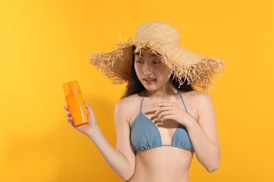 Photo of Beautiful young woman in straw hat holding sun protection cream on orange background, space for text