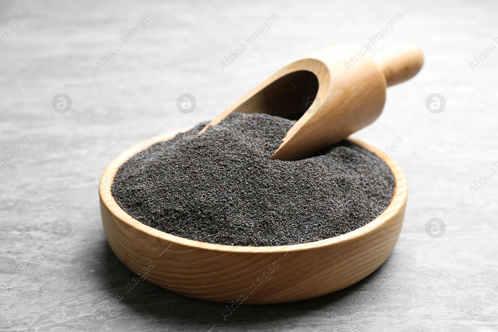 Photo of Poppy seeds and scoop in bowl on grey table