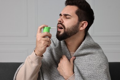 Photo of Young man using throat spray at home