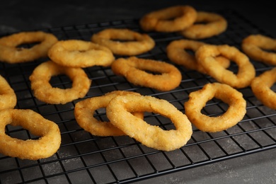 Photo of Cooling rack with fried onion rings on grey table