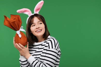 Photo of Easter celebration. Happy woman with bunny ears and wrapped egg on green background, space for text