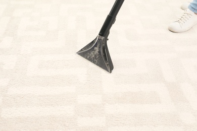 Woman removing dirt from carpet with vacuum cleaner indoors, closeup. Space for text