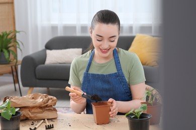 Happy woman planting seedling into pot at wooden table in room