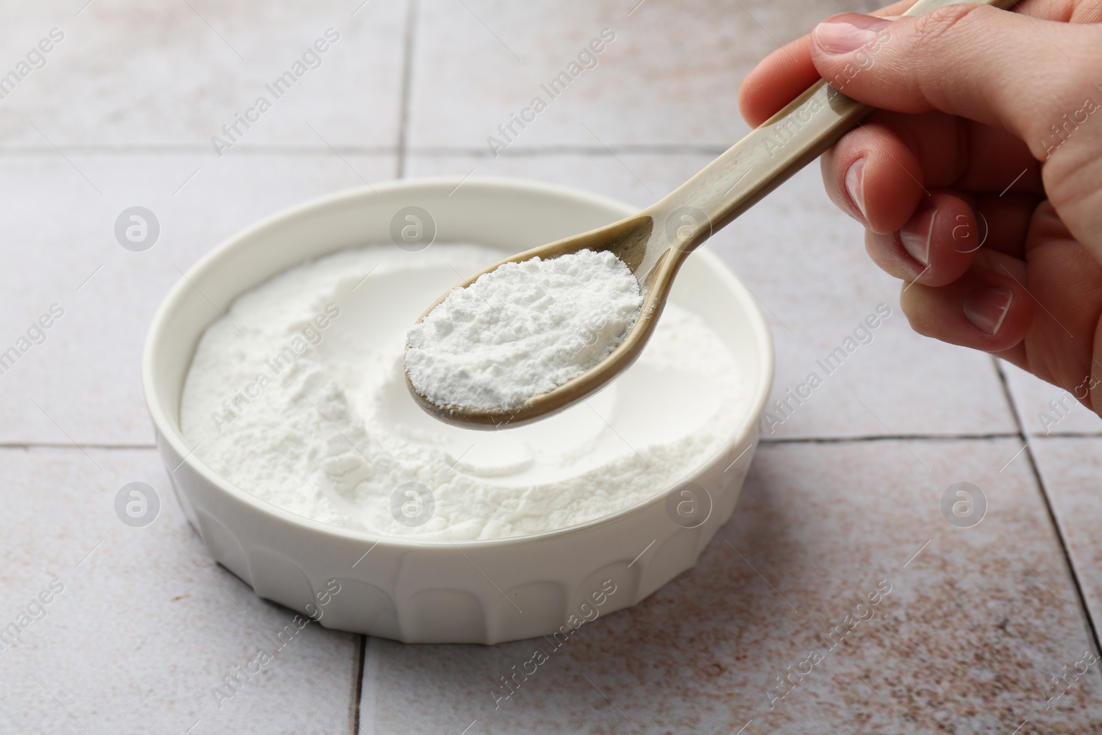 Photo of Woman taking baking powder with spoon from bowl at light tiled table, closeup