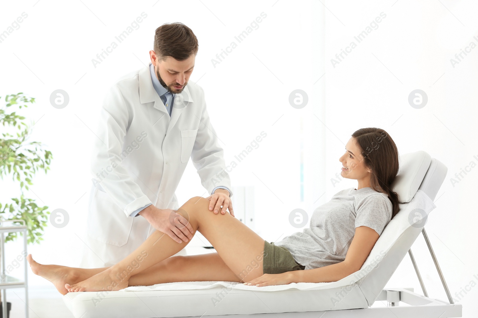 Photo of Doctor examining female patient with injured leg in clinic